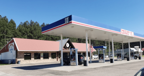 A gas station with a convenience store, featuring multiple fuel pumps and a clear blue sky in the background.