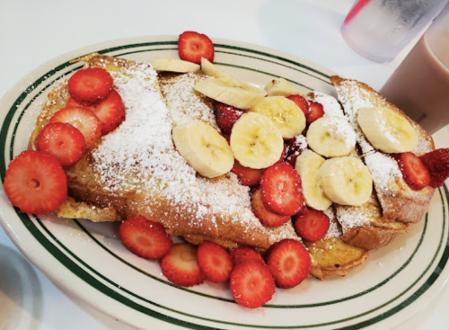 A plate of French toast topped with sliced strawberries, bananas, and powdered sugar.