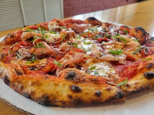 A close-up of a freshly baked pizza topped with tomato sauce, cheese, herbs, and slices of ham on a wooden table.