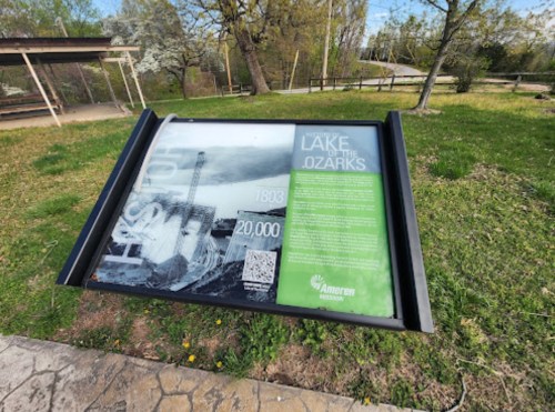 Informational sign about Lake of the Ozarks, featuring historical images and text, set in a grassy area.