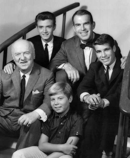 A black-and-white photo of five men posing together on a staircase, smiling at the camera.