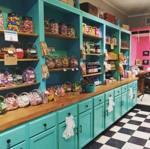 Colorful candy shop interior with jars of sweets on shelves and a wooden counter, featuring a checkered floor.