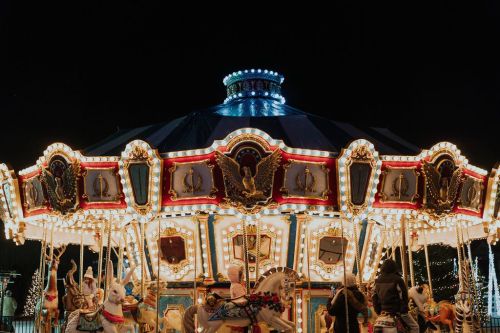 A brightly lit carousel at night, featuring ornate decorations and white horses, creating a festive atmosphere.