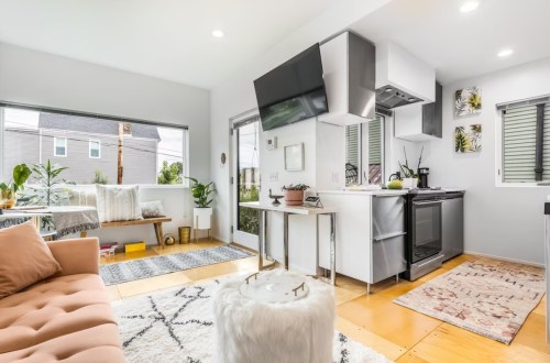 Bright, modern kitchen and living area with a cozy sofa, plants, and large windows letting in natural light.