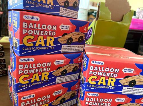A stack of colorful boxes for a balloon-powered wooden car toy, featuring playful graphics and warning labels.