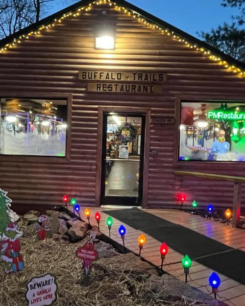 A cozy log cabin restaurant decorated with colorful lights and a sign warning of a Grinch nearby.