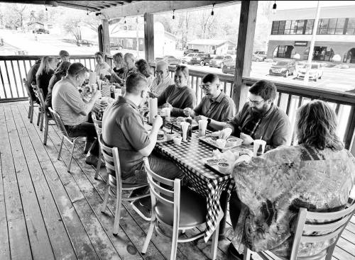 A group of people dining together at a long table on a porch, enjoying a meal in a casual setting.