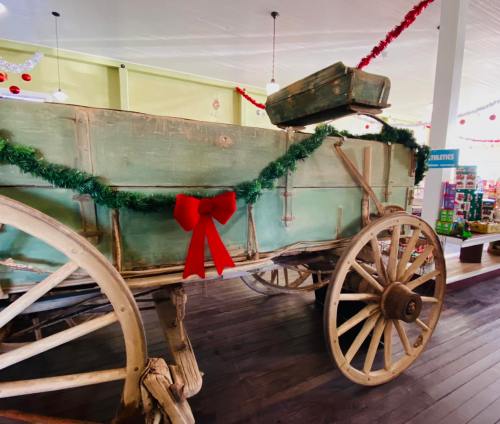 A vintage wooden wagon decorated with a green garland and red bow, set in a festive indoor space.