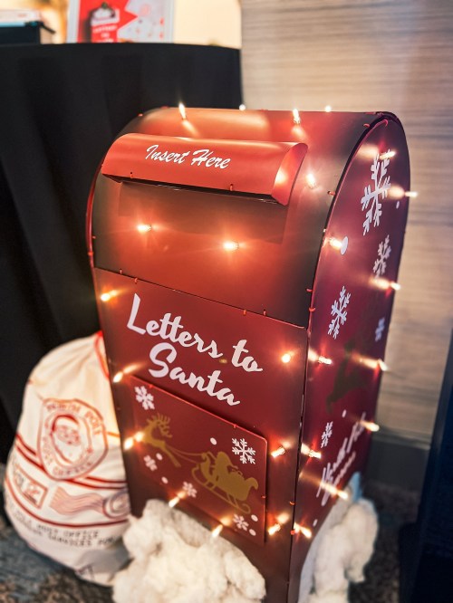 A festive red mailbox labeled "Letters to Santa," decorated with lights and surrounded by fluffy white snow.