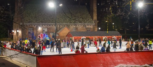 A bustling outdoor ice skating rink at night, with skaters enjoying the activity and festive lights in the background.