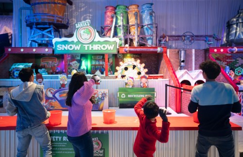 Four children play a game called "Santa's Snow Throw" at a colorful indoor amusement attraction.