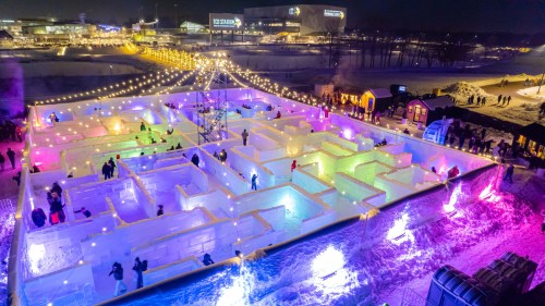 A colorful ice maze illuminated at night, with people exploring and festive lights in the background.