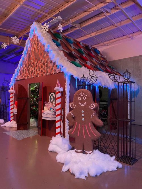 A festive gingerbread house display with candy decorations, snow, and a large gingerbread figure outside.