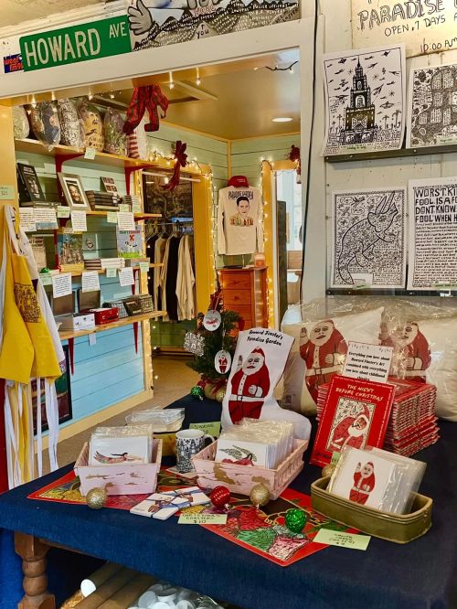 A cozy shop display featuring holiday cards, decorations, and festive items, with a sign for Howard Ave in the background.