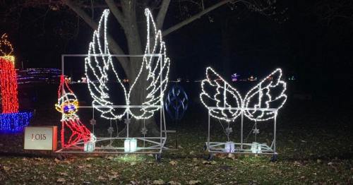 Two large illuminated angel wings made of white lights, set against a dark background with festive decorations.