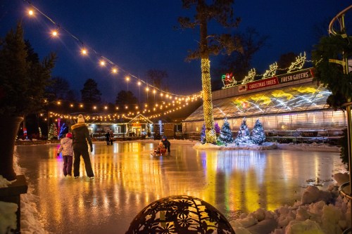 A festive outdoor ice skating rink at night, adorned with lights and Christmas decorations, with families enjoying the scene.