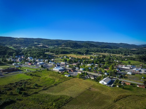 Aerial view of a small town surrounded by green hills and fields under a clear blue sky.