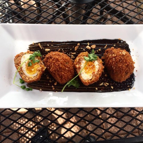 Three crispy fried balls with a golden yolk center, garnished with herbs, served on a dark sauce with crushed peanuts.