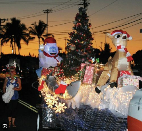 A festive parade float with inflatable characters, a Christmas tree, and gifts, set against a sunset backdrop.