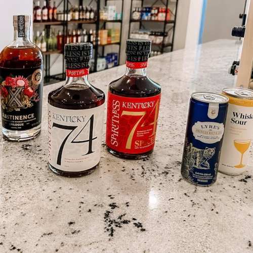 Bottles of Kentucky 74 spirits and Lyre's mixers on a granite countertop in a bar setting.