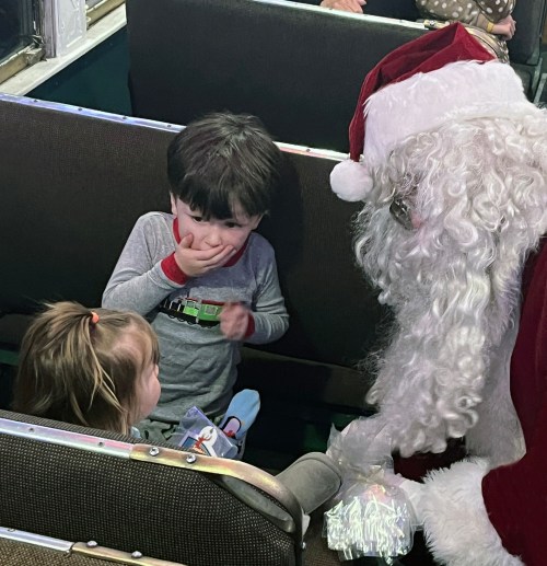 A Santa Claus figure interacts with two young children on a train, creating a festive atmosphere.