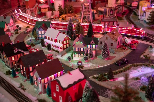 A festive miniature village with colorful houses, trees, and a train decorated with holiday lights.