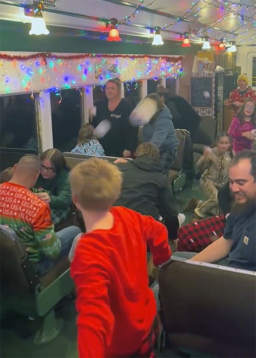 A festive train interior filled with people in holiday attire, enjoying a lively atmosphere with colorful lights.