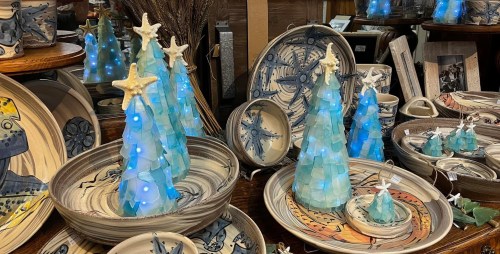 Decorative ceramic trees with blue lights among handcrafted pottery and plates on display.