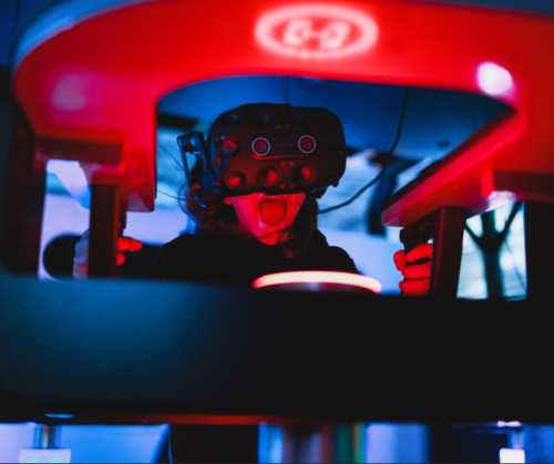 A person wearing a virtual reality headset, with a playful expression, surrounded by colorful lights.