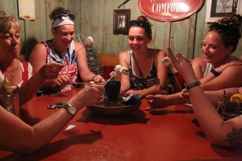 A group of friends around a table roasting marshmallows over a small fire, enjoying a fun gathering.