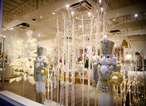 Two festive nutcracker figures stand among white trees and twinkling lights in a beautifully decorated holiday display.