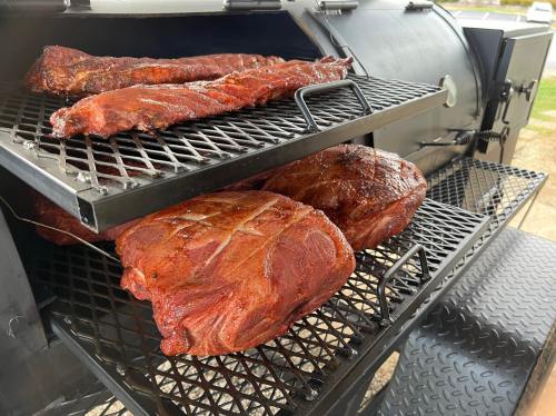 Smoked meats on a grill, including ribs and large cuts, cooking on metal racks inside a smoker.