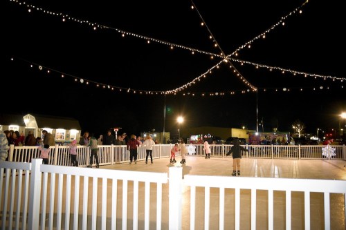 A festive outdoor ice skating rink at night, illuminated by string lights, with skaters and spectators enjoying the scene.
