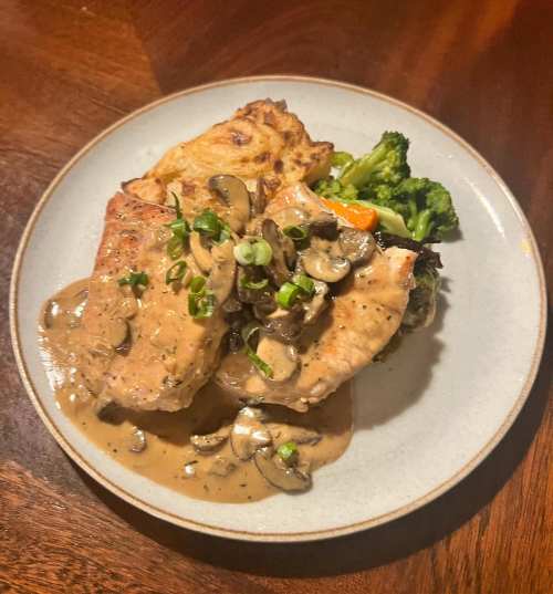 A plate of salmon with creamy mushroom sauce, served with broccoli and a side of baked potato.