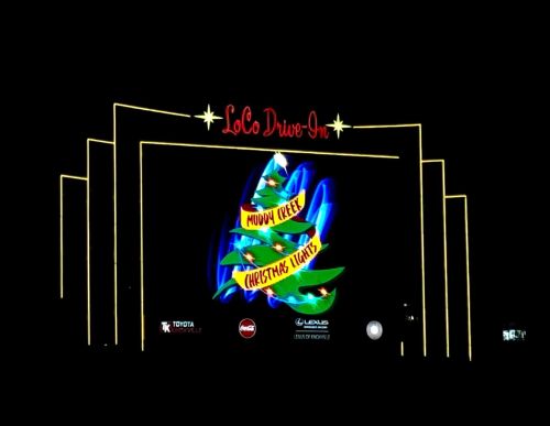 A brightly lit drive-in theater sign featuring a colorful Christmas tree and text for "Muddy Creek Christmas Lights."