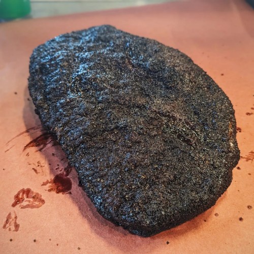 A burnt piece of food on a brown paper surface, showing a charred, blackened exterior.