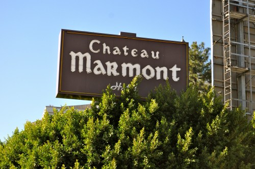 Sign for Chateau Marmont hotel partially obscured by greenery against a clear blue sky.