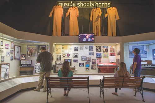 Visitors explore a music museum exhibit featuring memorabilia and a video display about Muscle Shoals.