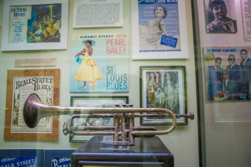 A vintage trumpet displayed in a glass case, surrounded by music posters and memorabilia.