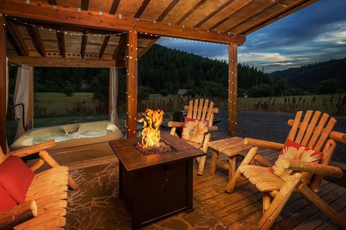 Cozy outdoor seating area with a fire pit, hot tub, and scenic mountain view at dusk.