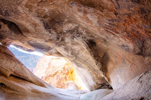 A cave interior with ancient rock art, featuring natural light illuminating the entrance and surrounding rocky textures.