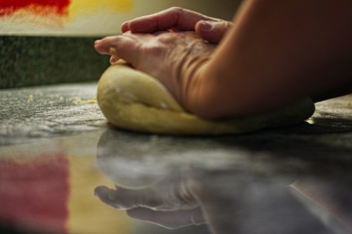 A person's hands knead dough on a floured countertop, with a reflection visible on the surface.
