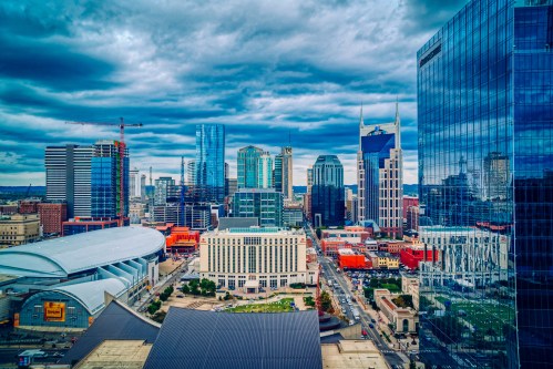 Aerial view of a city skyline featuring modern skyscrapers and a cloudy sky, with a mix of urban architecture.
