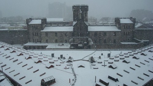 A historic building covered in snow, with rooftops and a snowy landscape under a heavy snowfall.