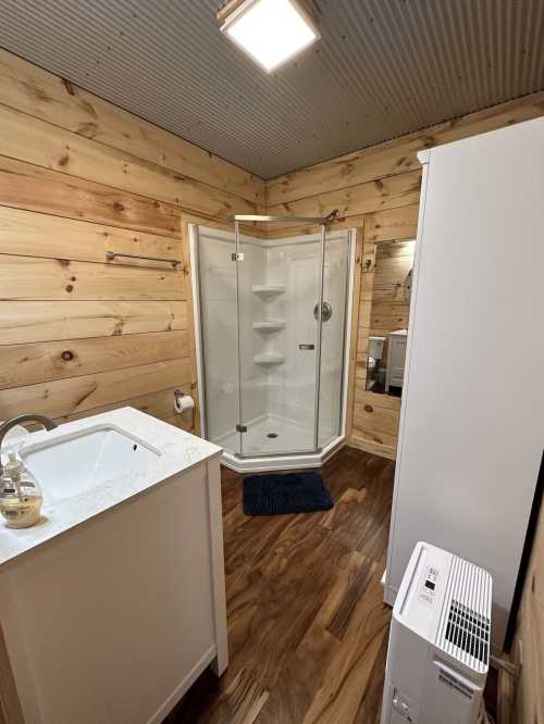 A cozy bathroom featuring a shower, sink, wooden walls, and a small heater on the floor.