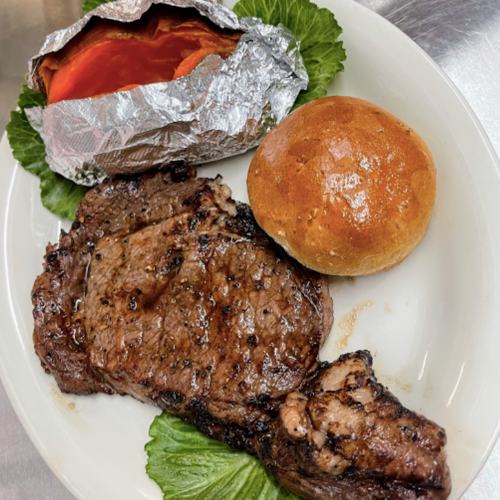 A plate featuring a grilled steak, a baked potato wrapped in foil, a roll, and lettuce leaves.