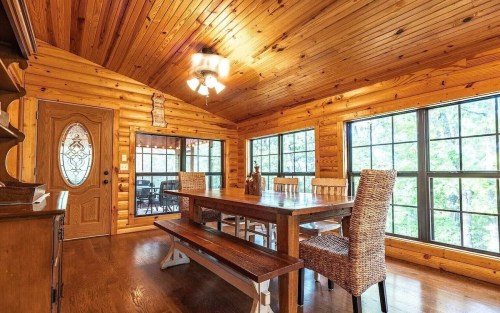Cozy wooden dining area with a large table, woven chairs, and large windows overlooking a natural view.