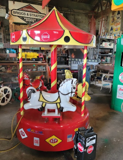 A vintage carousel with colorful horses, set in a rustic garage filled with nostalgic items.