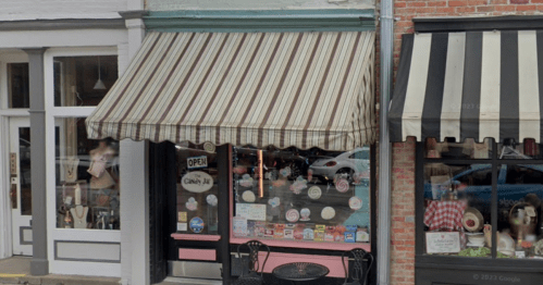 A quaint shop with a striped awning, displaying an "Open" sign and colorful window decals.