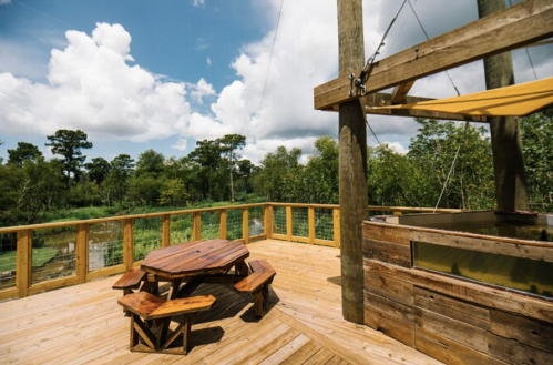 A wooden deck with a picnic table overlooks a lush green landscape under a partly cloudy sky.